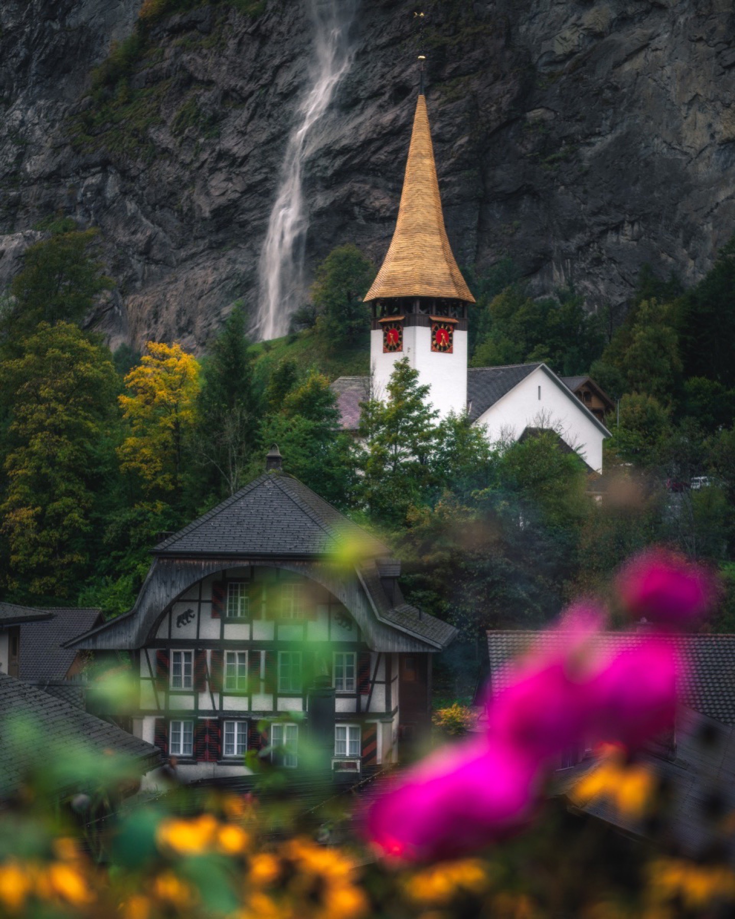 Swiss village church and waterfall photographed through out-of-focus flowers
