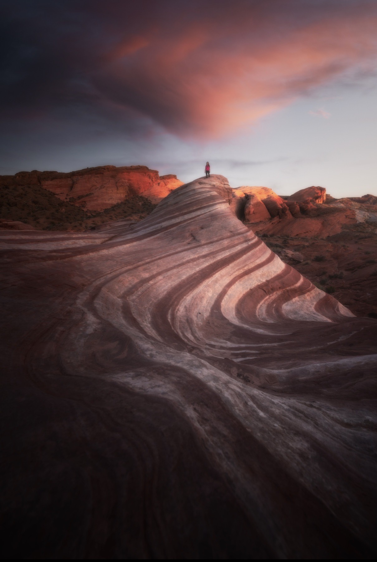 Person standing on curving red sandstone beneath a pink cloud