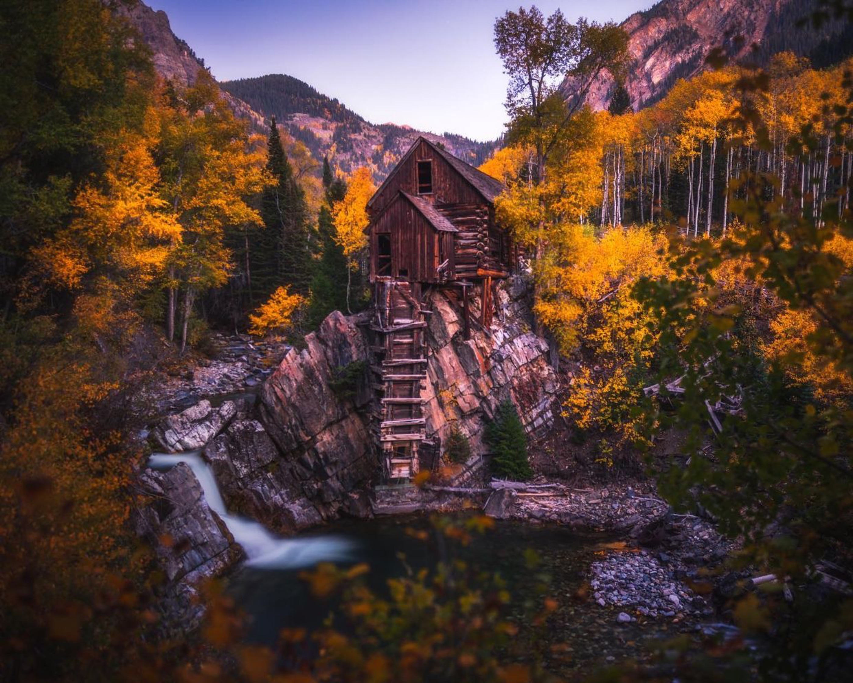 Historic wooden structure above moving water surrounded by Colorado fall color