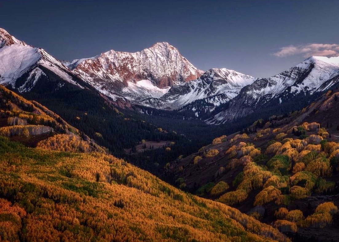 Snow-covered Colorado mountains above layered orange and gold aspen valleys