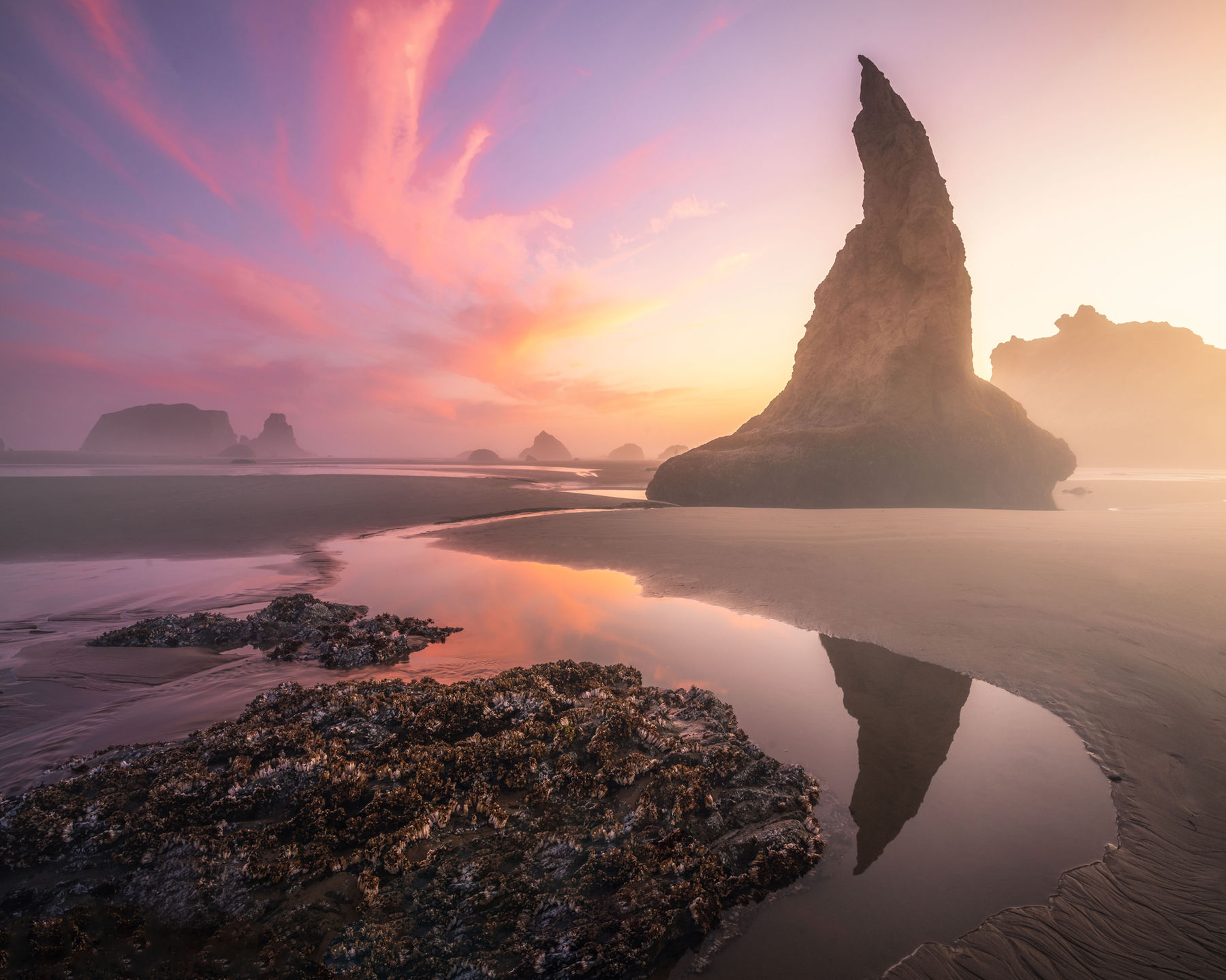 Bandon sea stacks reflected in wet sand beneath a colorful sunset