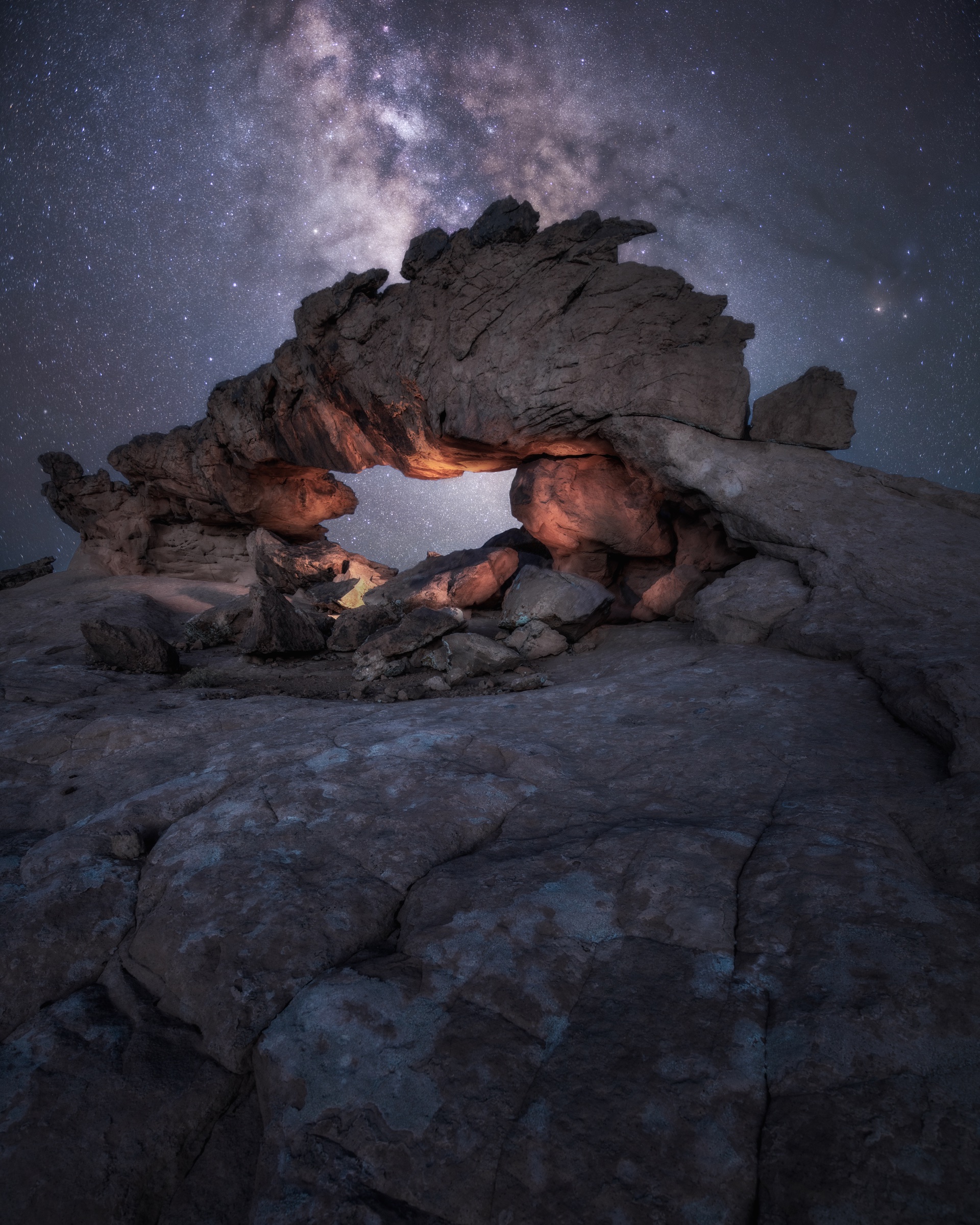 Milky Way above a roughly fifty-foot-long natural rock arch lit in separate sections