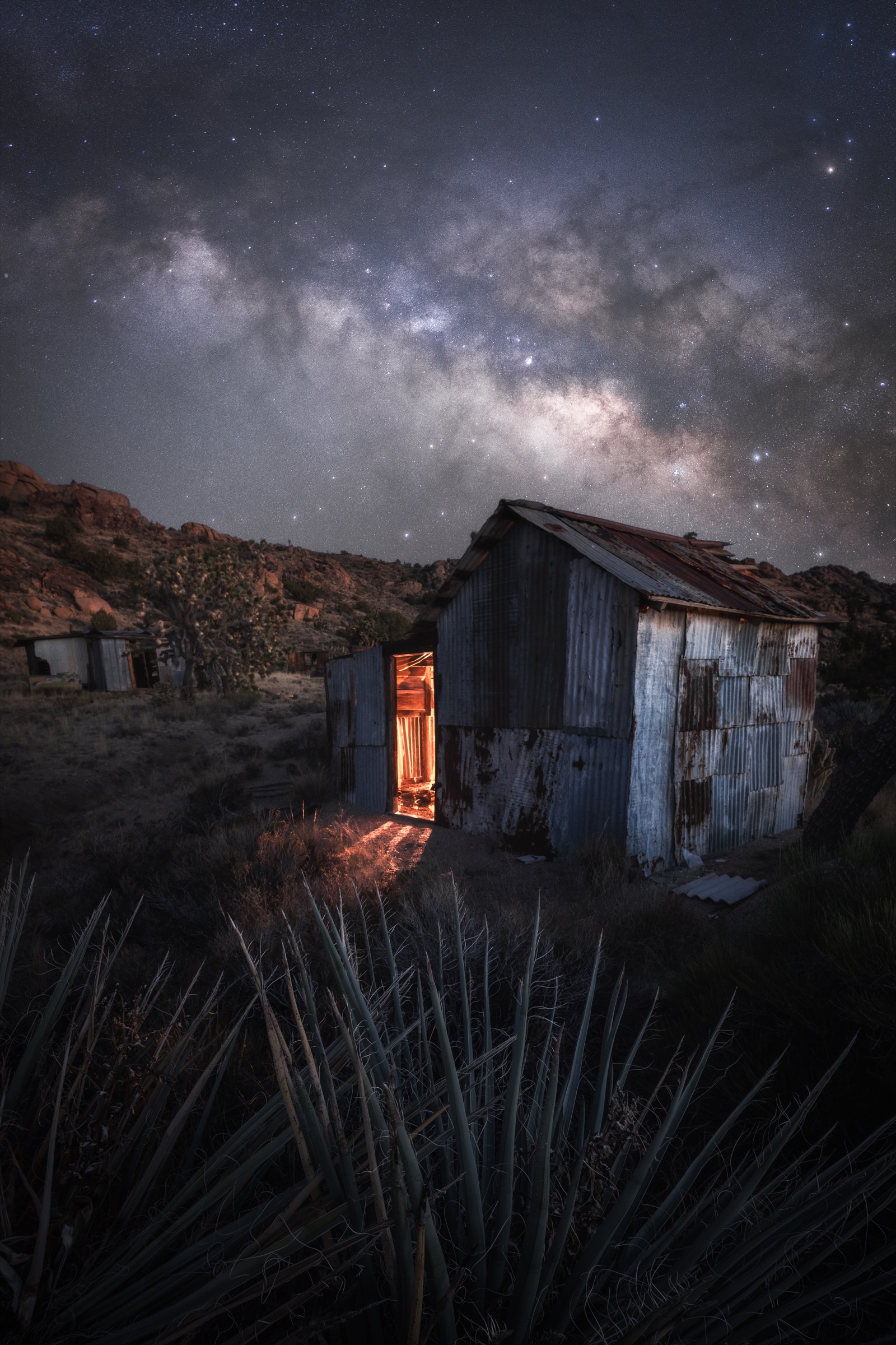 Warm light glowing through an abandoned Mojave ghost-town shack beneath the Milky Way