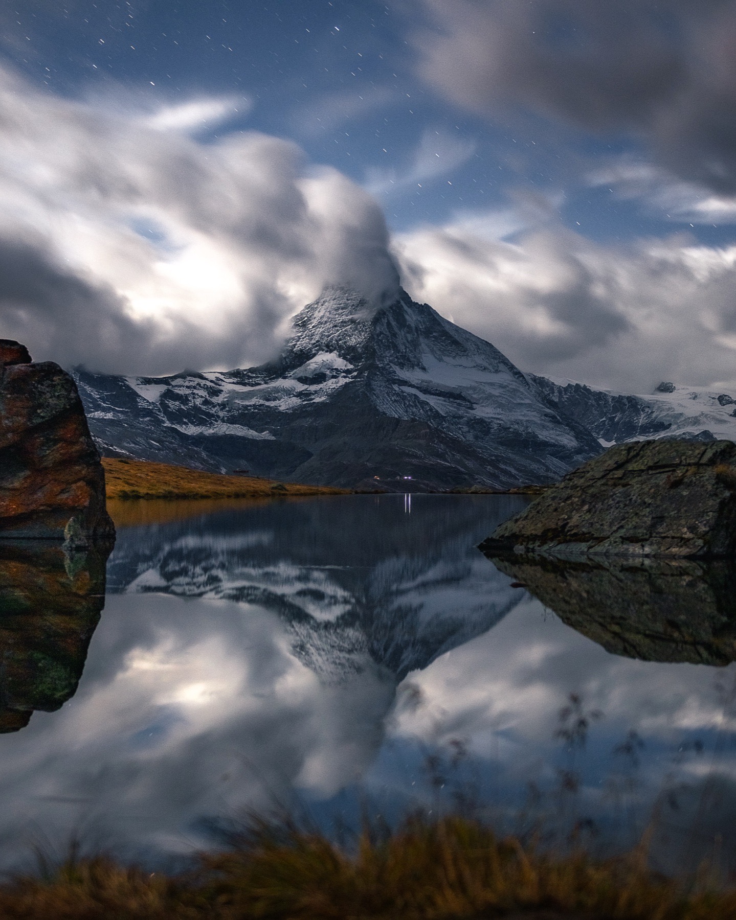 Moonlit Matterhorn reflected in a lake beneath moving clouds and stars
