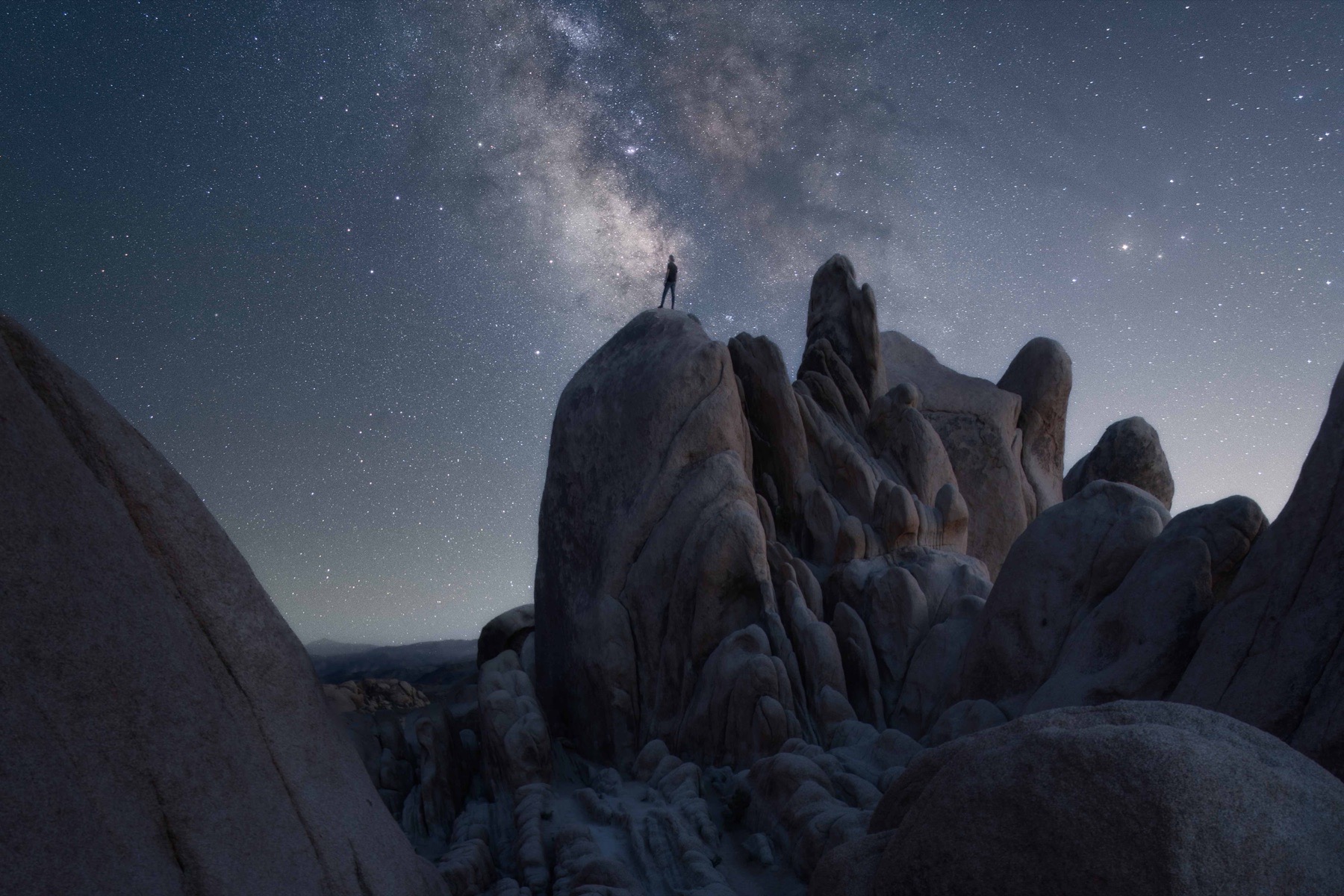 Milky Way above side-lit granite rock formations with a photographer silhouetted on a boulder