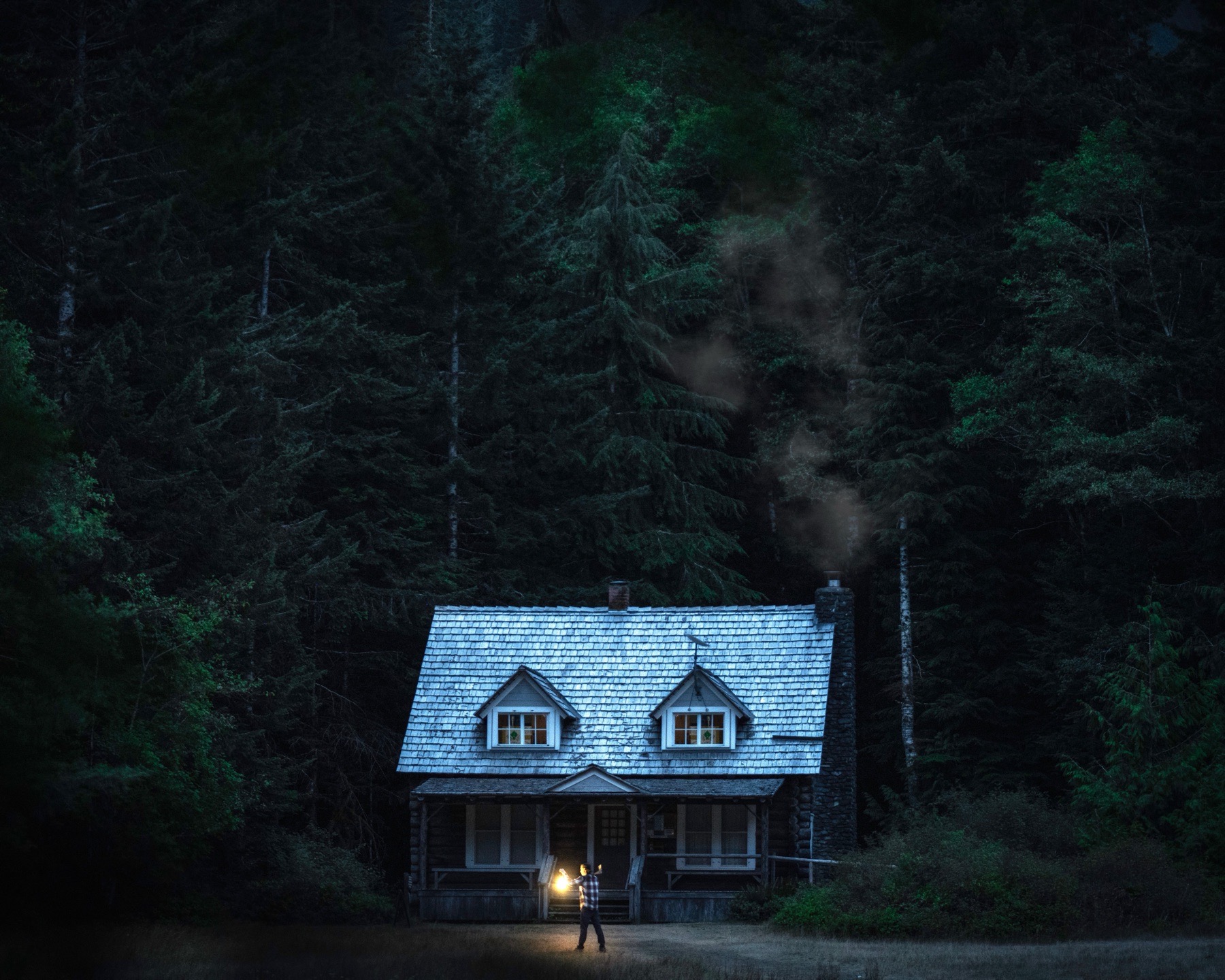 Lone cabin in the forest at dusk with warm lantern glow in front.