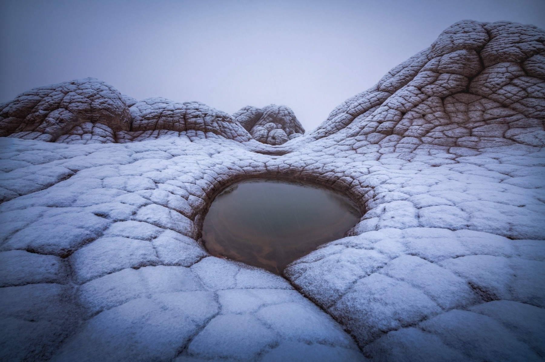 Snow-covered White Pocket sandstone surrounding a small circular pool
