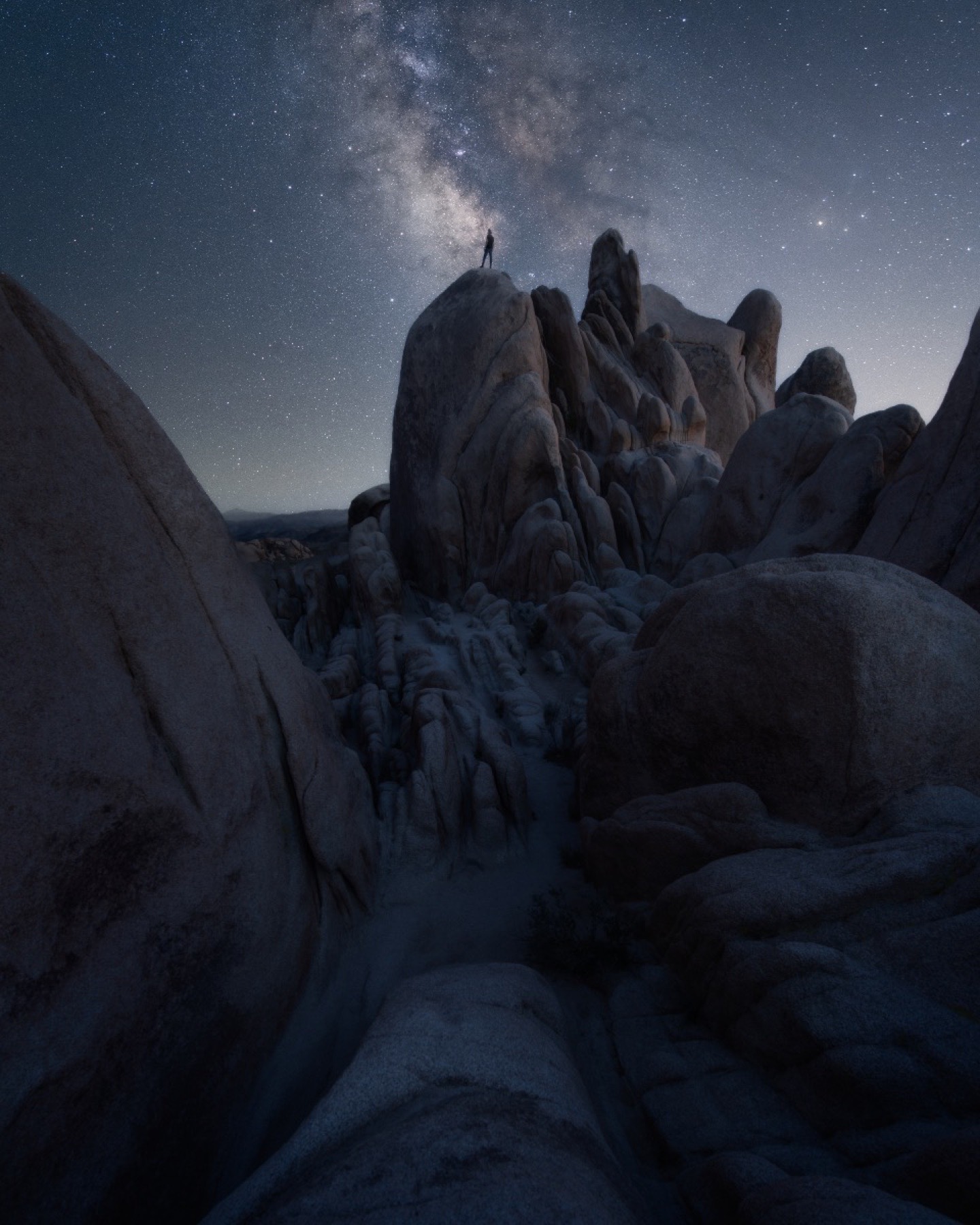 Small person standing on Joshua Tree boulders beneath the Milky Way