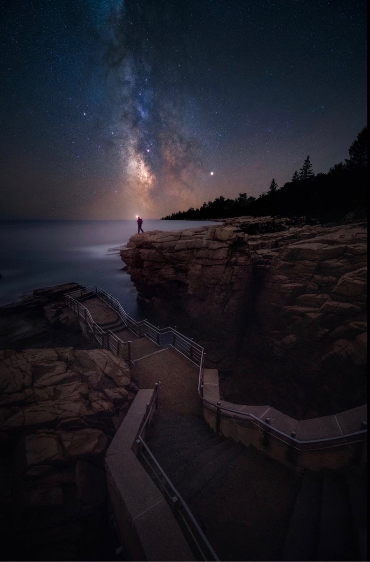 Milky Way above a rocky Acadia coast with stairs leading to a silhouetted person